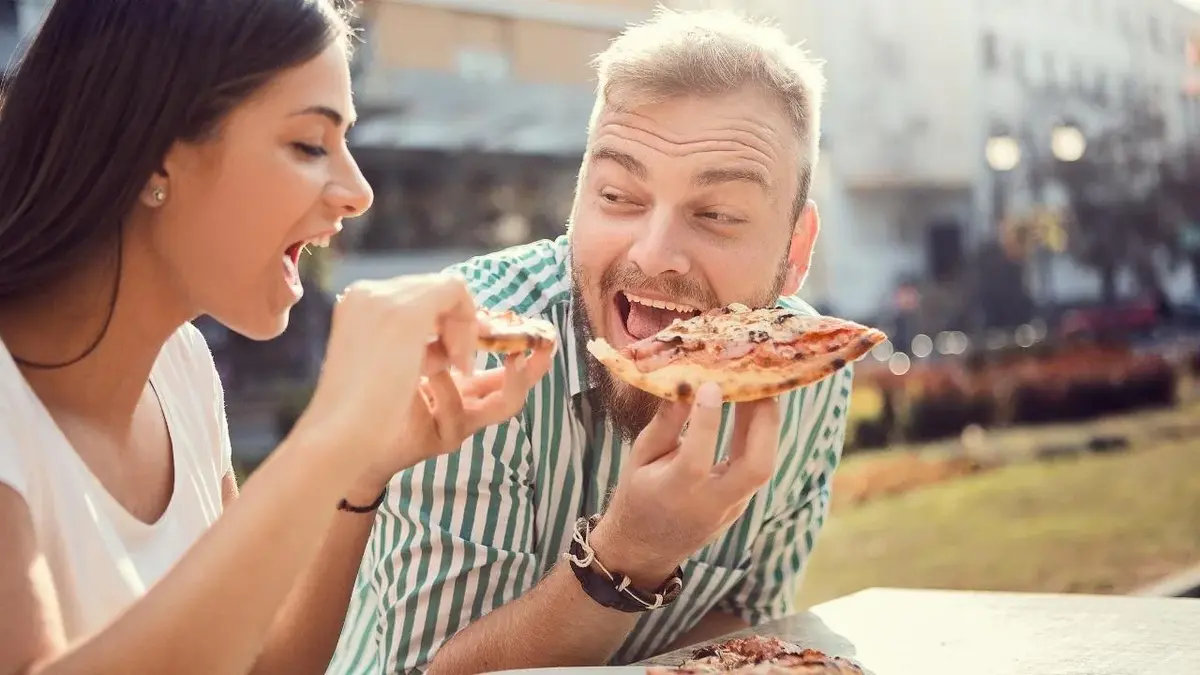 Dziewczyna i chłopak zjadają pizzę podczas majówki.