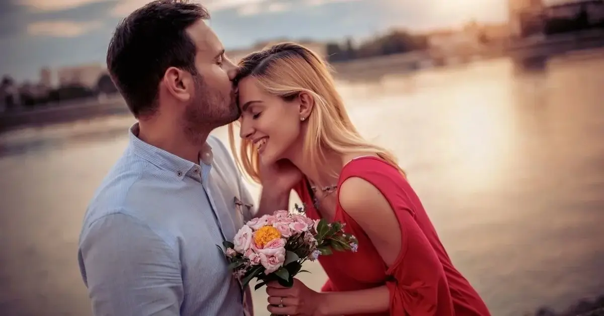 Zakochani kobieta i mężczyzna podczas majówki na tle zachodzącego słońca. Kobieta trzyma kwiaty.