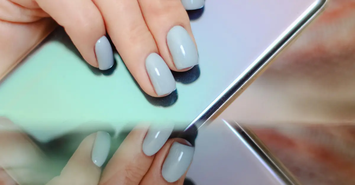 Kobiece dłonie z perfekcyjnym manicure lakierem Makear trzymają telefon w obudowie miętowo-fioletowe