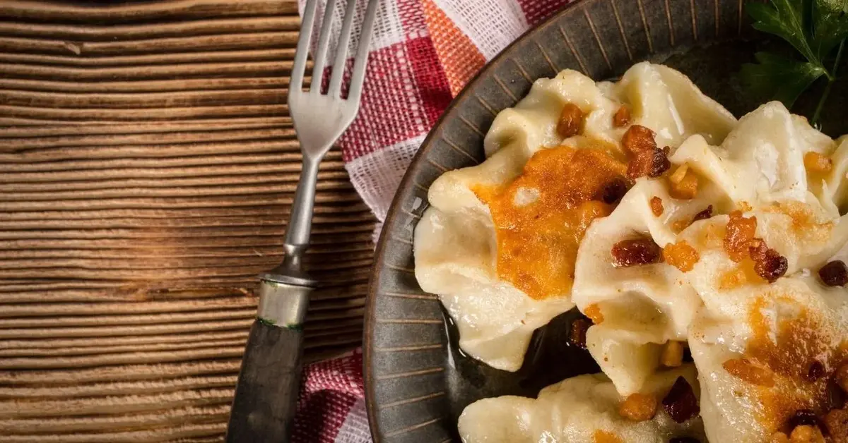 Pierogi z mięsem i dynią podane z brązowym talerzu, okraszone skwarkami