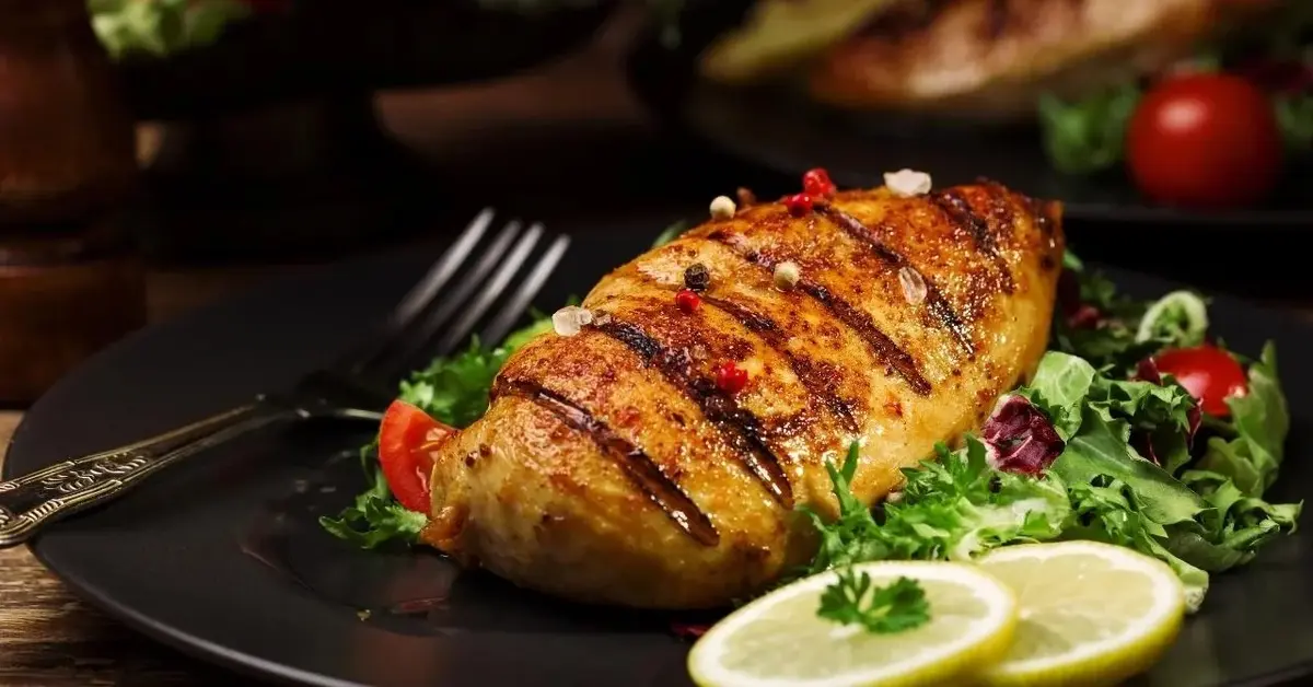 Grillowana pierś z kurczaka, na talerzu. Obok mięsa jest sałata i cytryna.