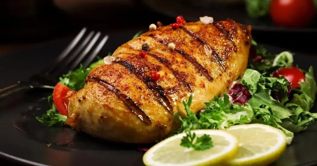 Grillowana pierś z kurczaka, na talerzu. Obok mięsa jest sałata i cytryna.
