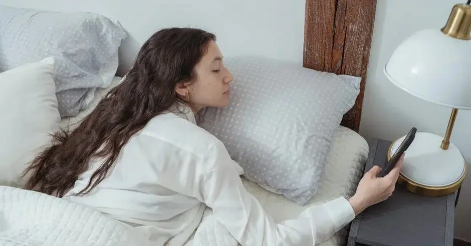 Nastolatka leżąca w łóżku w pokoju nastolatka w jasne pościeli spogląda na telefon