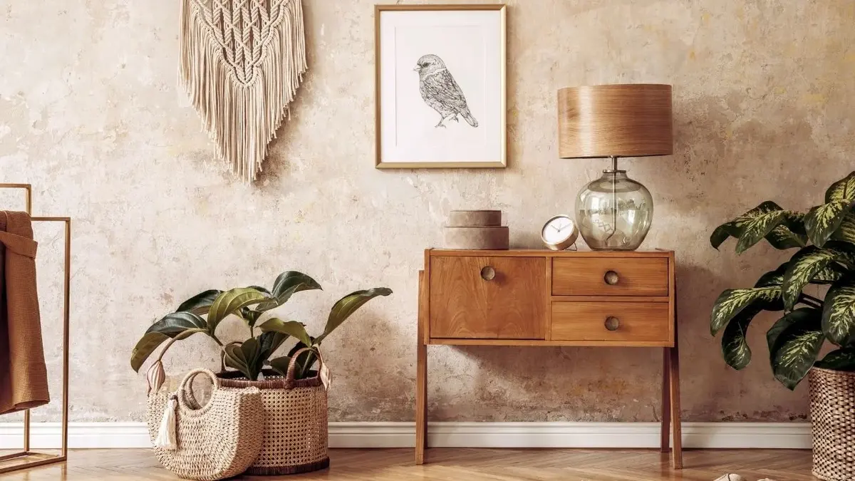 Pokój wabi-sabi z drewnianym stolikiem, szklaną lampą, plecionymi koszami, makramą i obrazkiem na postarzanej ścianie