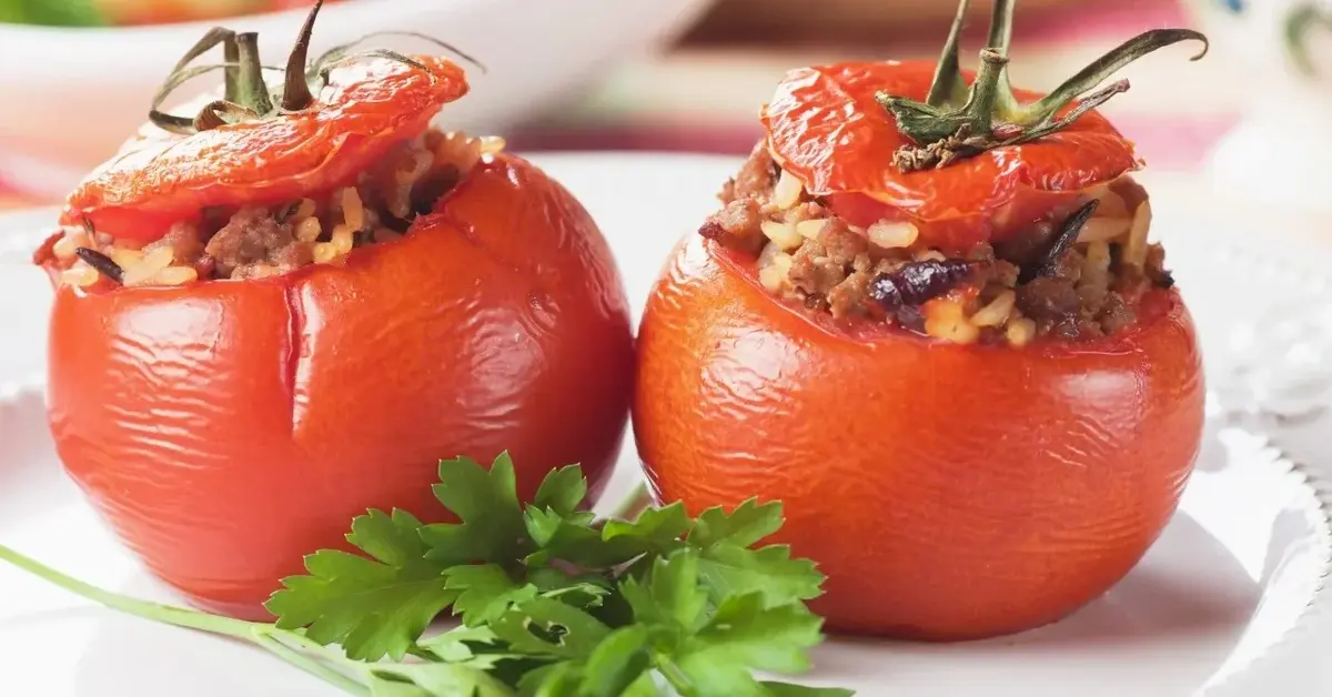 dwa pomidory faszerowane z przykrywkami obok natka pietruszki na talerzu