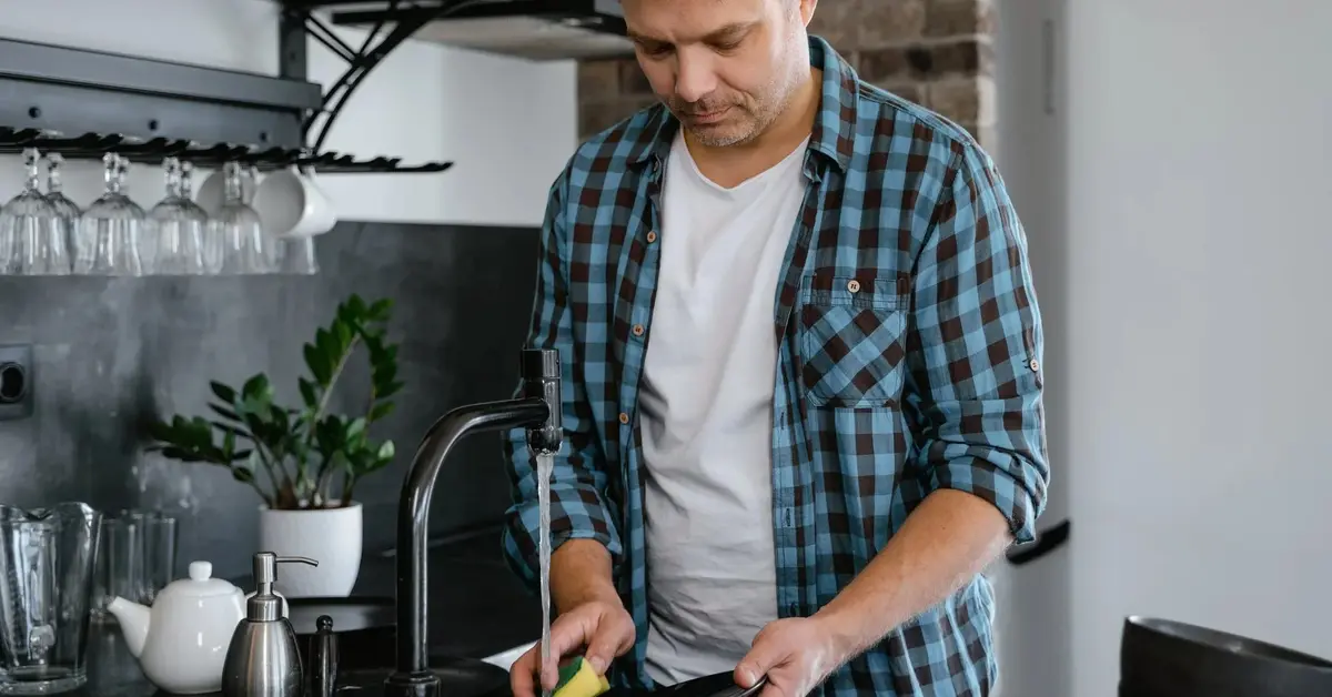 Mężczyzna w kraciastej koszuli myje naczynia w kuchni