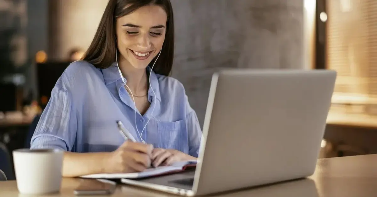 Uśmiechnięta kobieta o długich czarnych włosach pracuje online w kawiarni z kubkiem kawy i rozłożonym komputerem