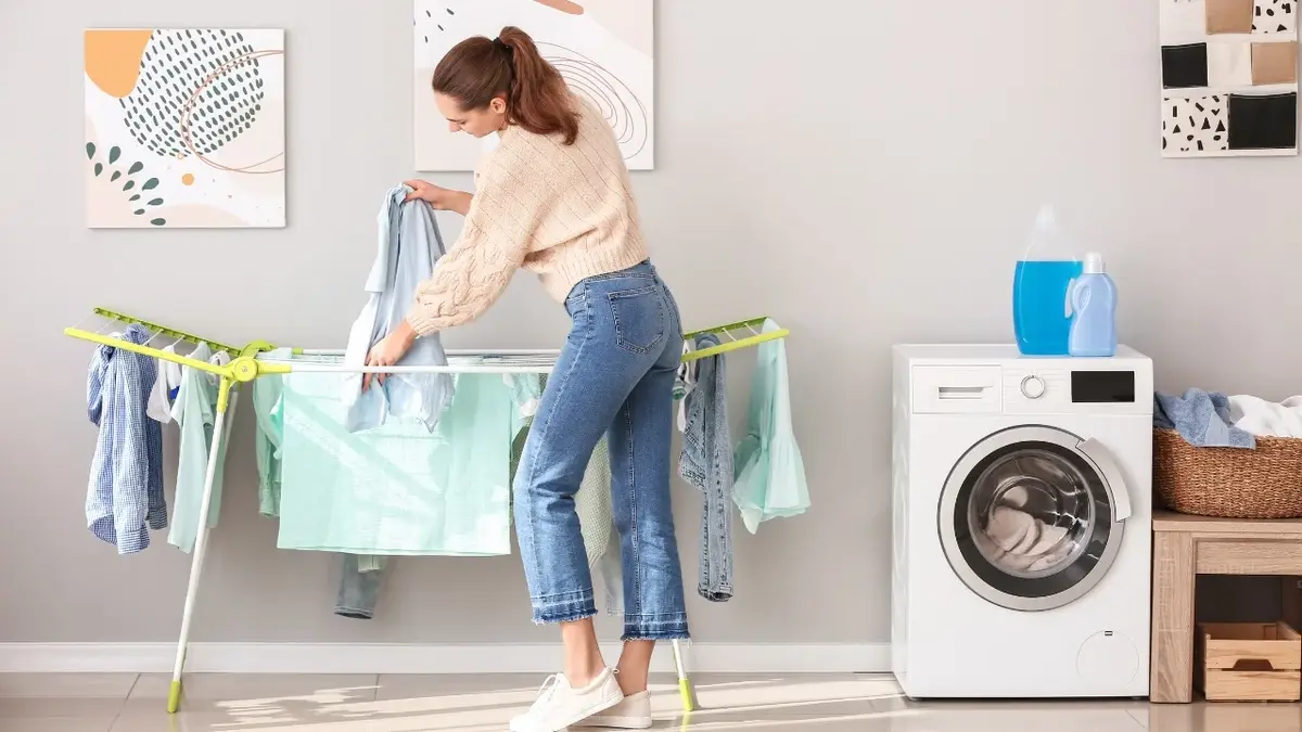 kobieta rozwiesza pranie na domowej suszarce, obok stoi pralka