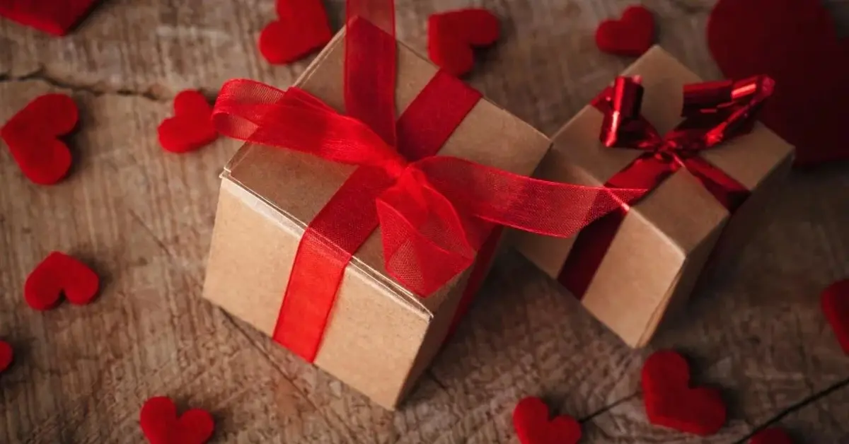 Prezenty na walentynki obwiązane czerwoną wstążką. Obok czerwone serduszka.