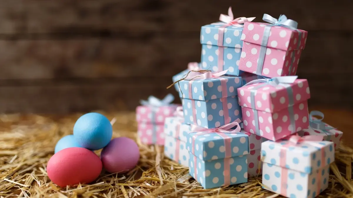 Prezenty na Wielkanoc dla dzieci i kolorowe jajka leżące na sianie.