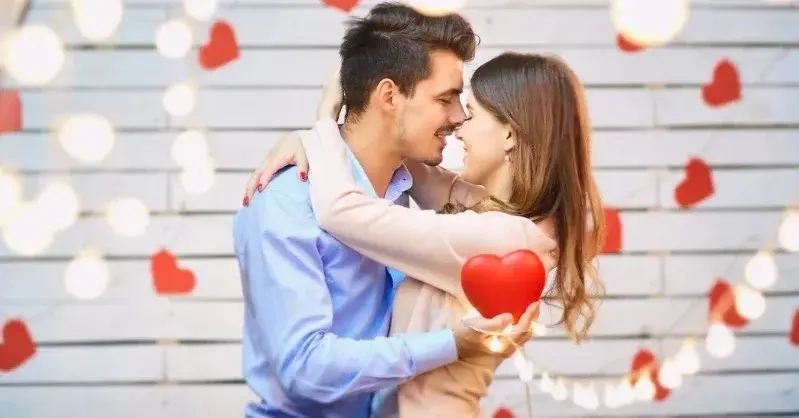 Całująca się para w objęciu na tle białej ściany ozdobionej lampkami oraz czerwonymi sercami walentynkowymi