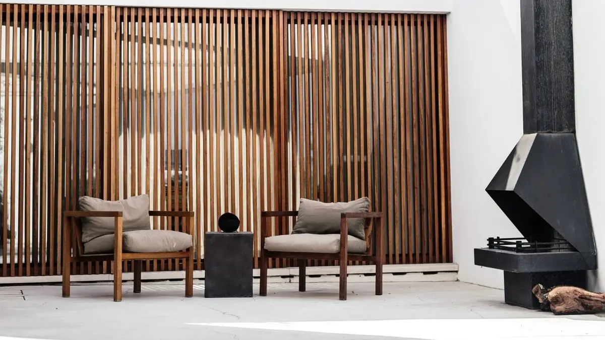 Drewniane przepierzenie z lameli, na jego tle dwa szare fotele i stolik
