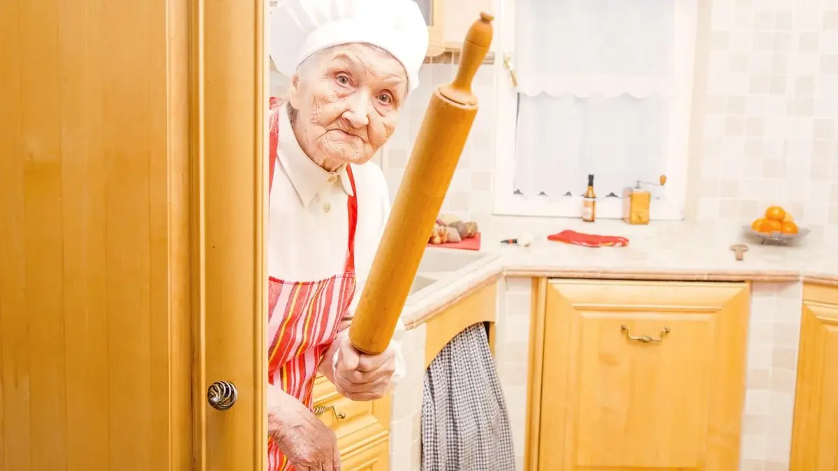 Babcia w ubraniu kuchennym z wałkiem w ręce szykuje się do gotowania według przepisu babci