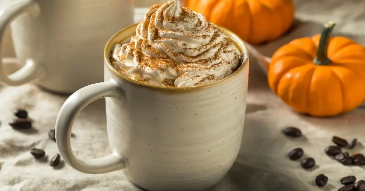 pumpkin spice latte w kubku z bitą śmietaną wokół dynie i ziarna kawy