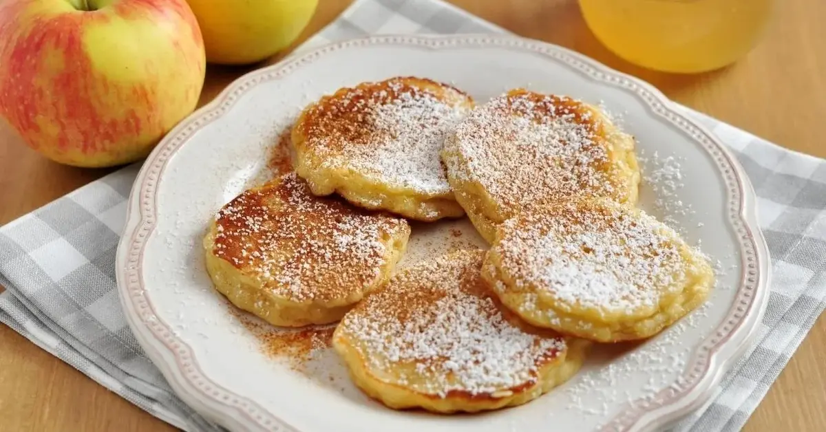 Racuchy z jabłkiem na talerzu posypane cukrem pudrem.