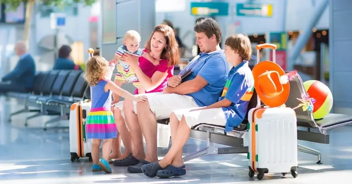 Rodzinna podróż na wakacje - rodzice z dziećmi siedzą na ławce, obok stoi walizka