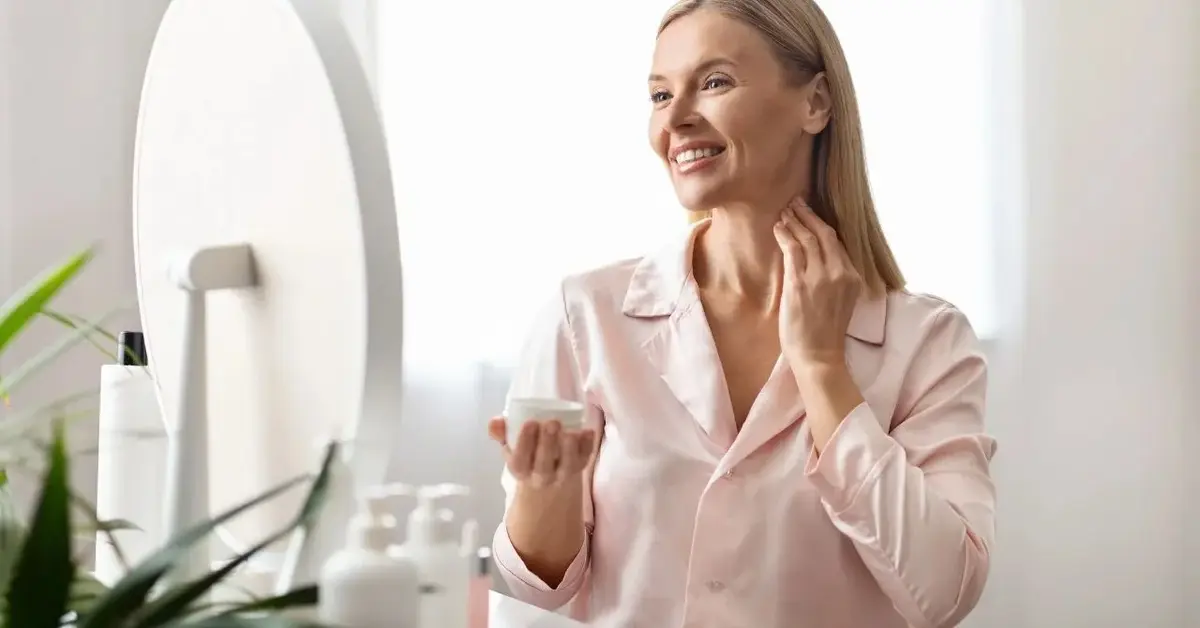 Kobieta po 50 roku życia nakładająca krem na twarz i dekolt