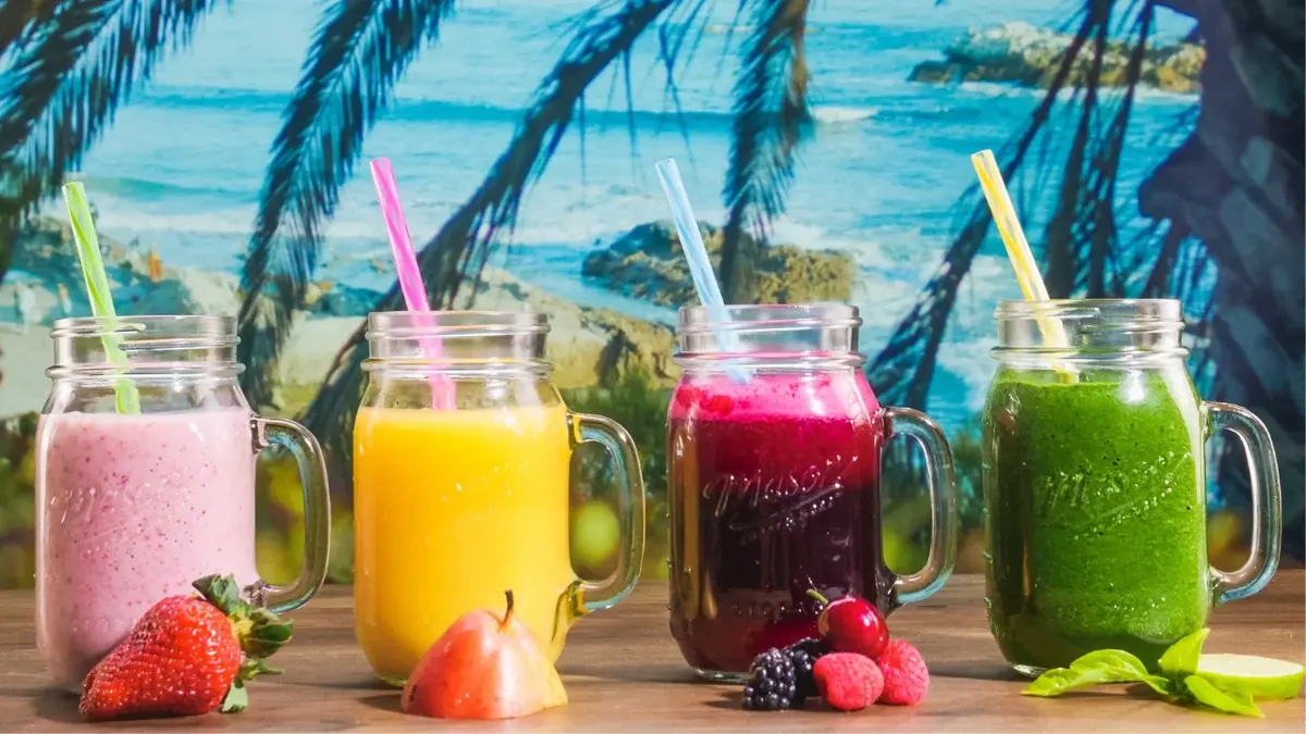 cztery szklanki z koktajlami przed nimi owoce w tle palmy i błękitna woda