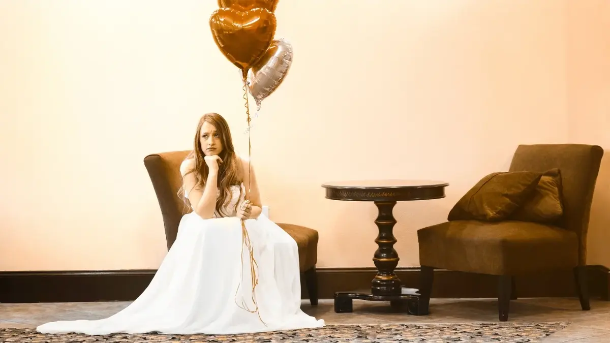 Smutna panna młoda siedzi na krześle i trzyma w ręku balony na sznurku.