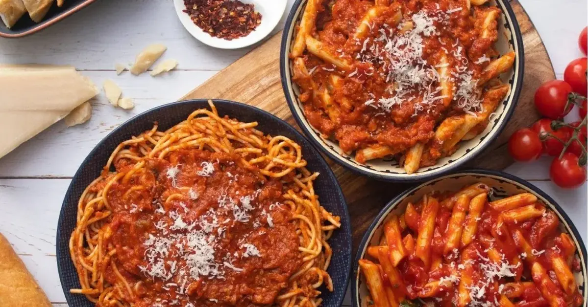 spaghetti bolognese w trzech talerzach na desce z tyłu ser i przyprawy w miseczce obok pomidorki koktajlowe