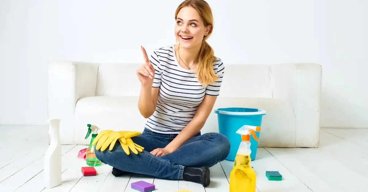 kobieta siedzie na białej podłodze wśród narzędzi i środków do sprzątania