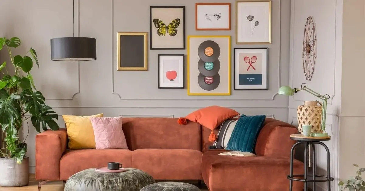 Kanapa w kolorze terakoty na tle szarej ściany z plakatami i grafikami