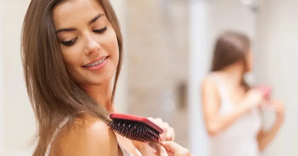 Kobieta po użyciu suchego szamponu rozczesuje włosy przed lustrem w łazience