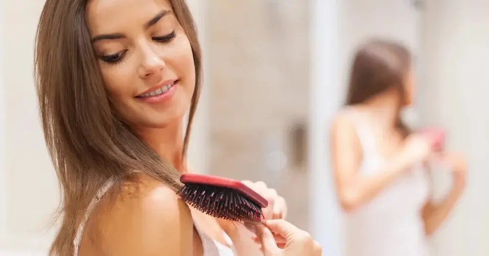 Kobieta po użyciu suchego szamponu rozczesuje włosy przed lustrem w łazience