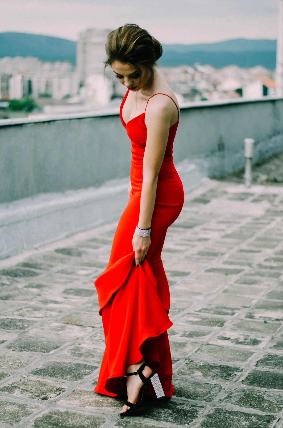 Piękna kobieta z włosami w kok prezentuje nogę w wysokim czarnym obcasie ubrana w czerwoną sukienkę wieczorową