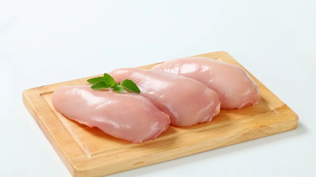 Surowe filety z kurczaka leżą na drewnianej desce do krojenia i są udekorowane listakmi.
