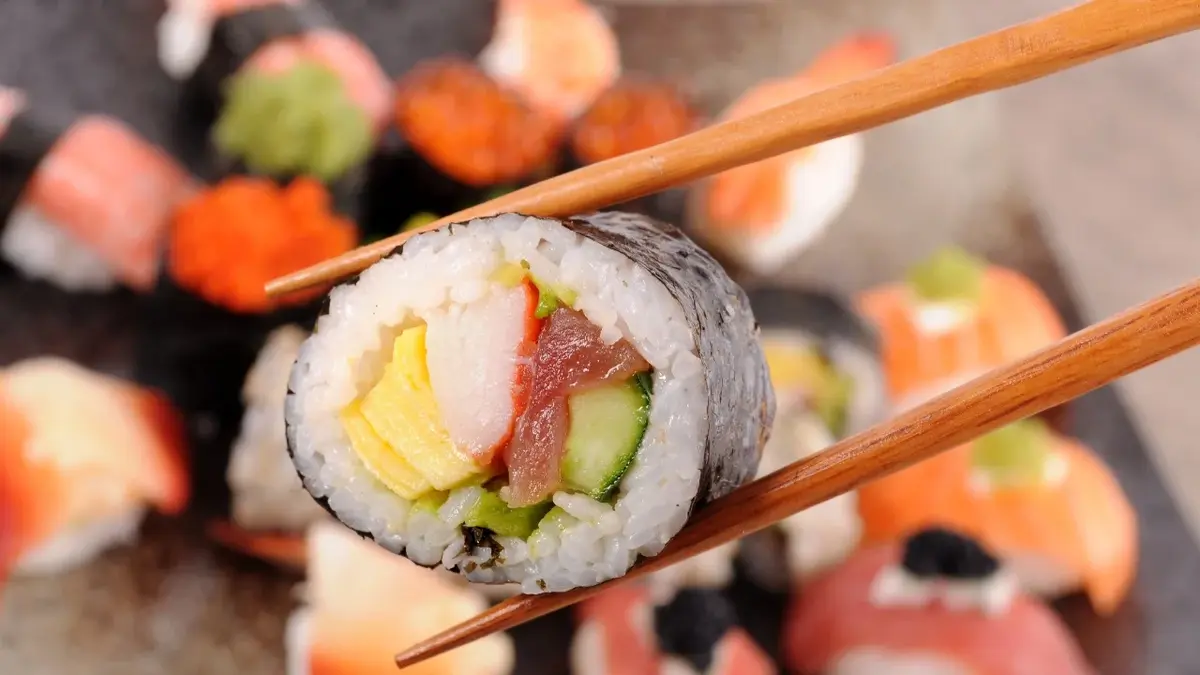 sushi jedna rolka trzymana w pałeczkach w tle więcej sushi