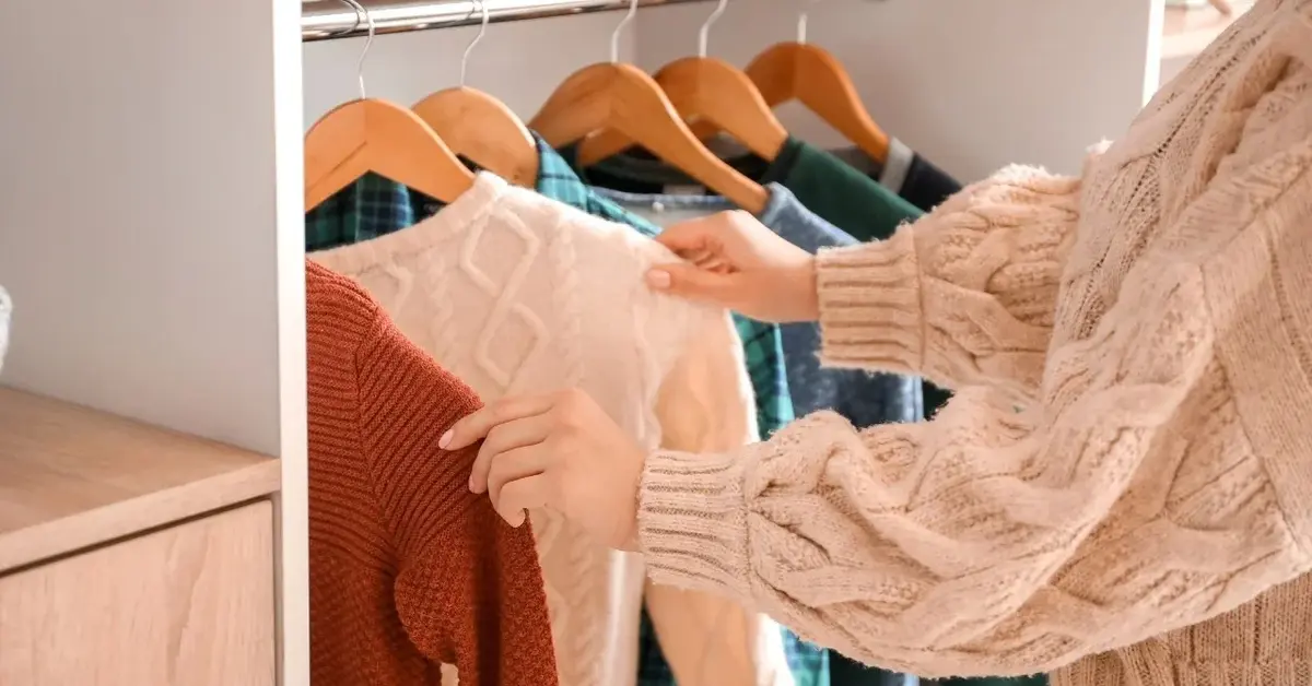 kobieta przegląda swetry wiiszące w szafie
