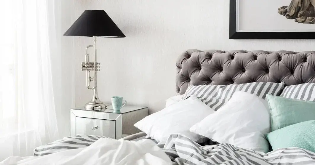 Elegancka sypialnia utrzymana w bieli i szarościach z lustrzaną szafką nocną przy łóżku 