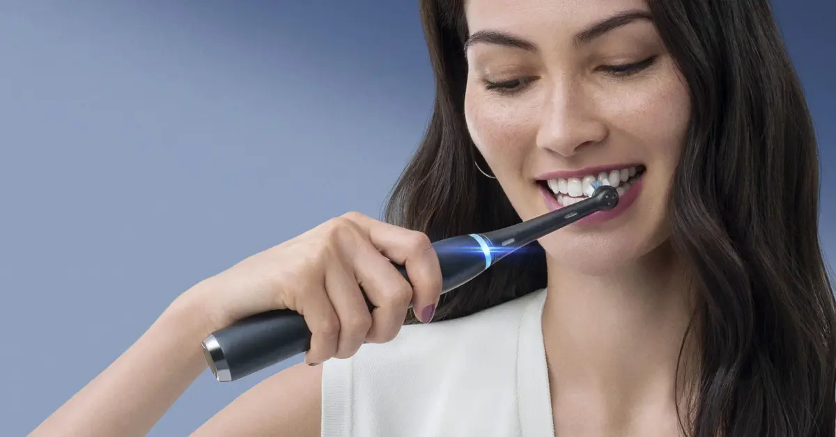 Szczęśliwa kobieta o długich czarnych włosach w białej koszulce myje zęby elektryczną szczoteczką rotacyjną oral b