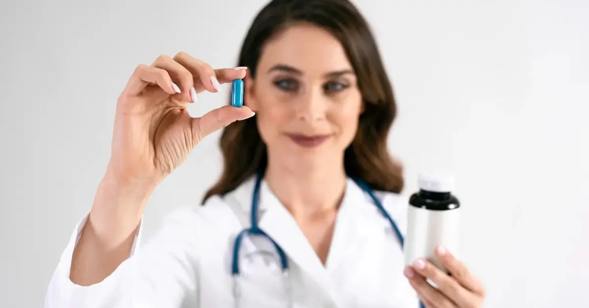 Lekarka w białym kitlu i ze stetoskopem na szyi w wyciągniętej ręce w palcach trzyma niebieską tabletkę