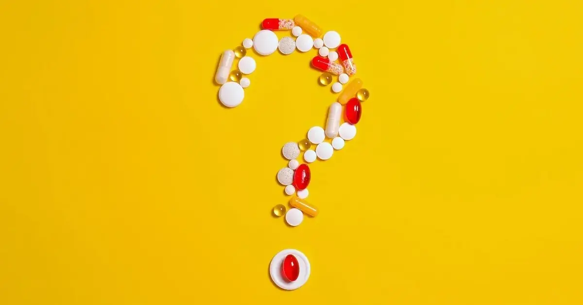 Na jaskrawożółtym tle znak zapytania pytajnik ułożony z białych i czerwonych tabletek