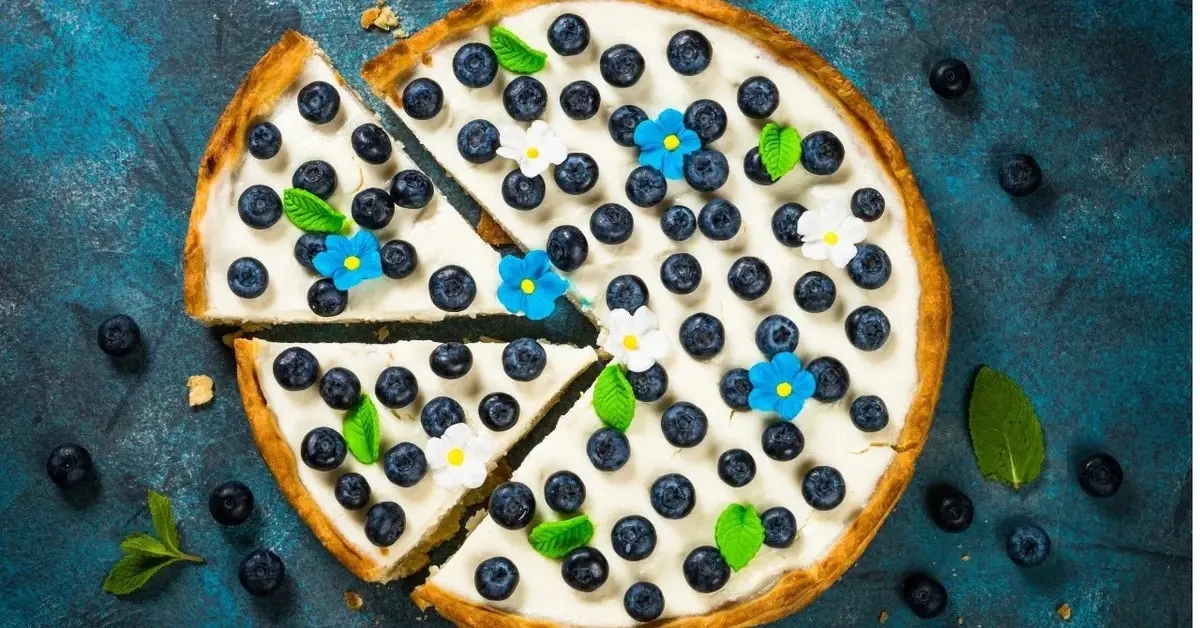 tarta z kremem mascarpone borówkami niebieskimi kwiatami i zielonymi listkami