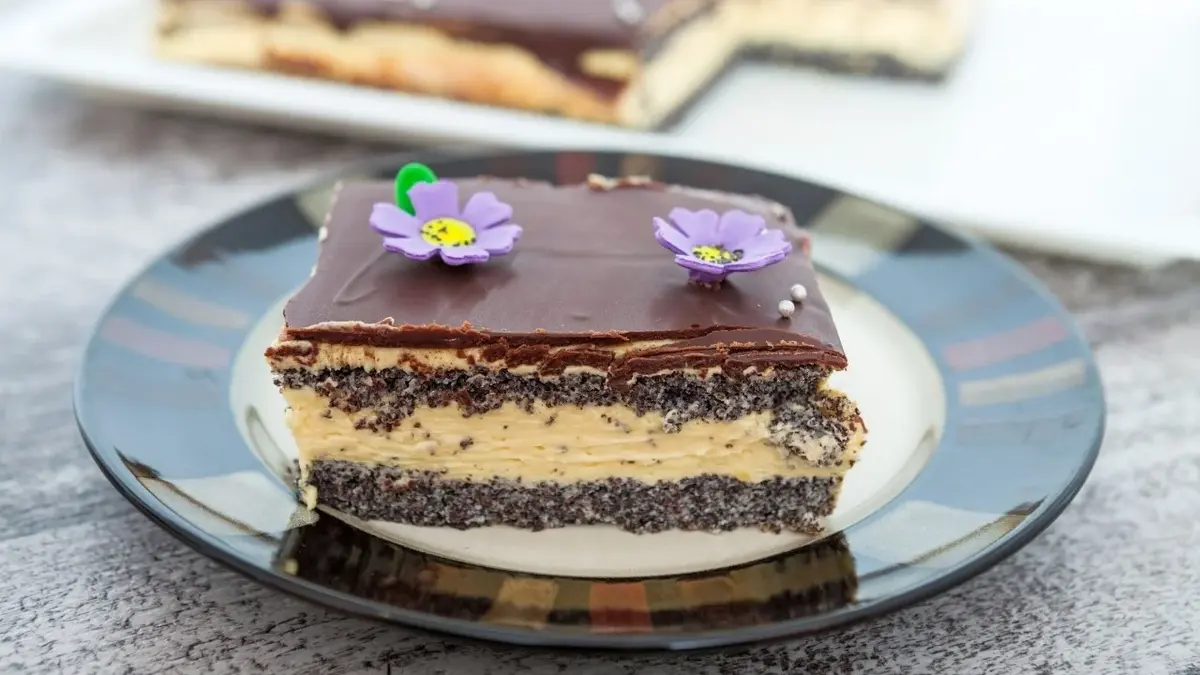 tort makowy z kremem polany czekoladową polewą z kwiatuszkami na talerzu