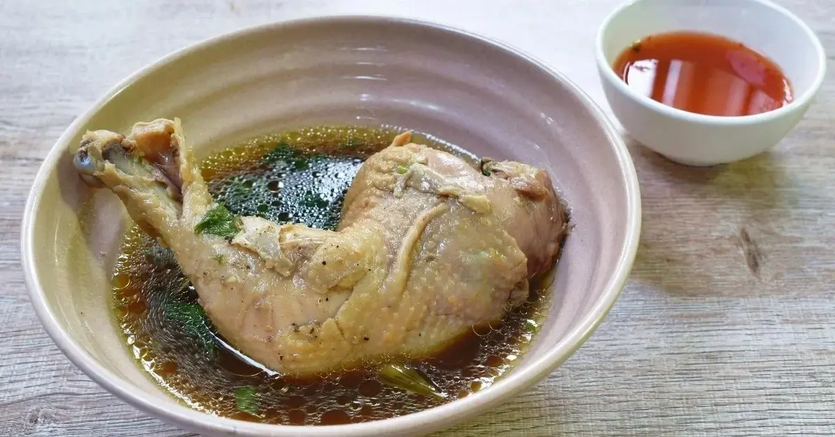 Gotowane udko z kurczaka leży w misce z rosołem.