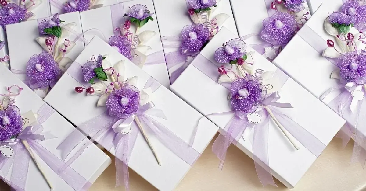 Prezenty dla gości weselnych w białych opakowaniach ozdobionych fioletową dekoracją.