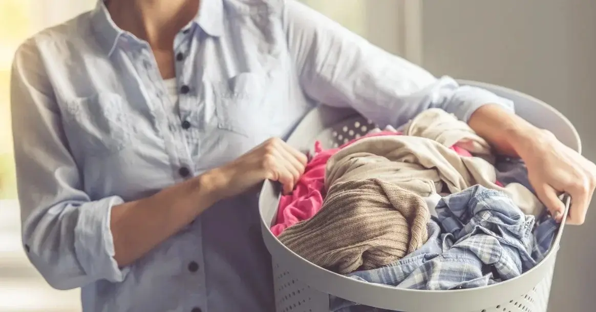 Uśmiechnięta kobieta z praniem, z którego usunęła zapach potu.