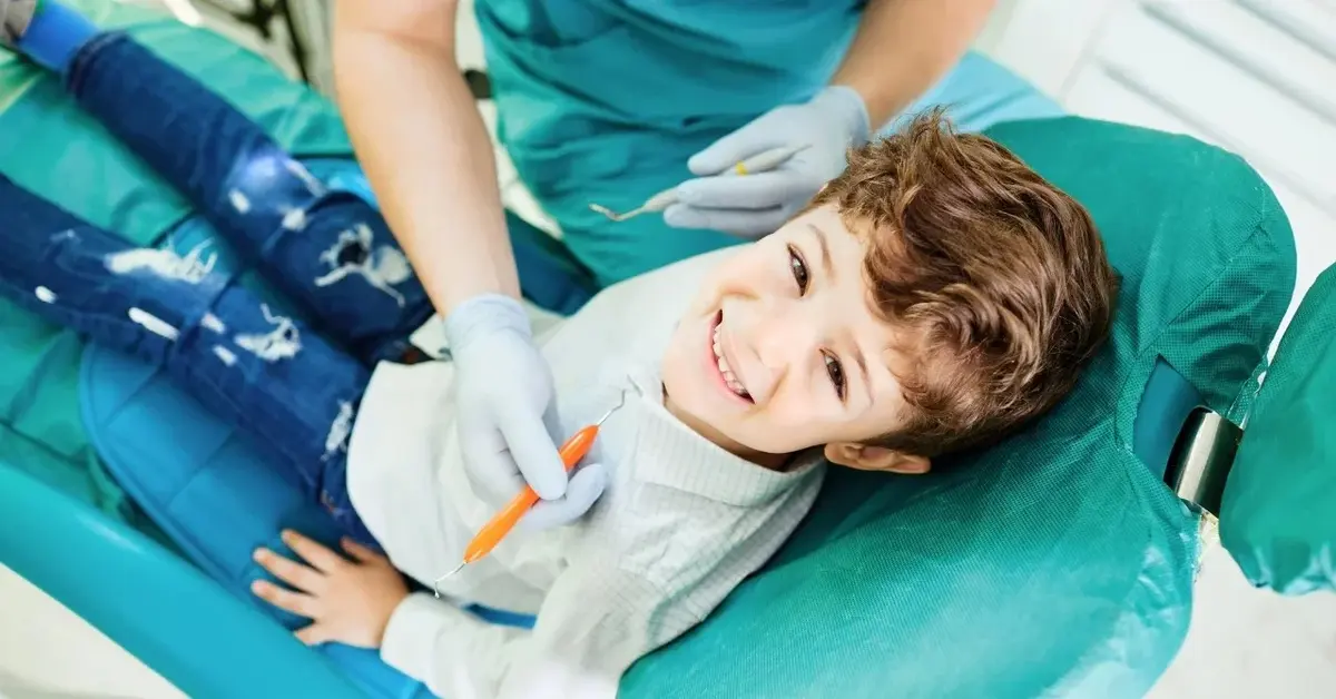 Uśmiechnięty chłopiec siedzi na fotelu dentystycznym.