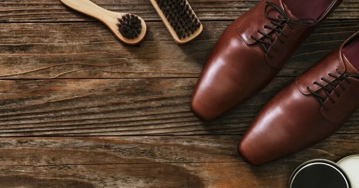 Drewniane narzędzia do polerowania butów wraz z brązowymi skórzanymi eleganckimi butami męskimi na drewnianym tle