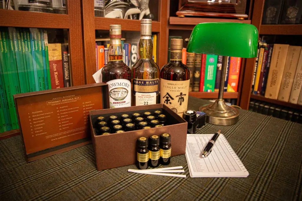 Zestaw próbek do analizy i degustacji whisky w ciemnym drewnianym gabinecie na biurku z zieloną lampą