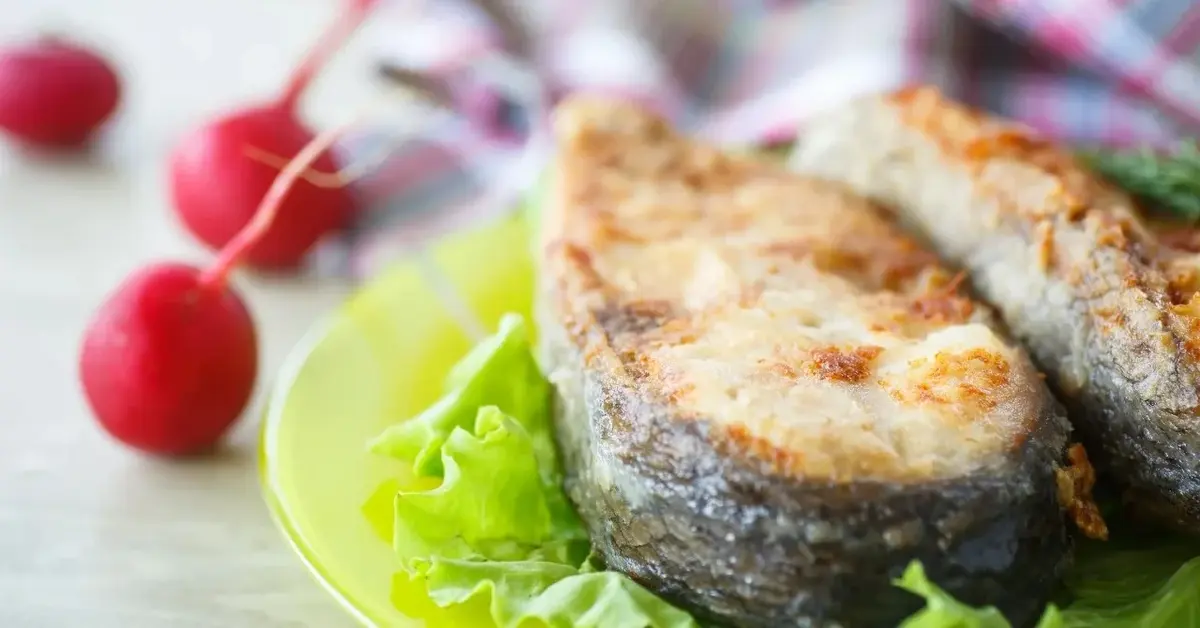 Wigilijny karp smażony na talerzu na liściu sałaty. W tle rzodkiewki.