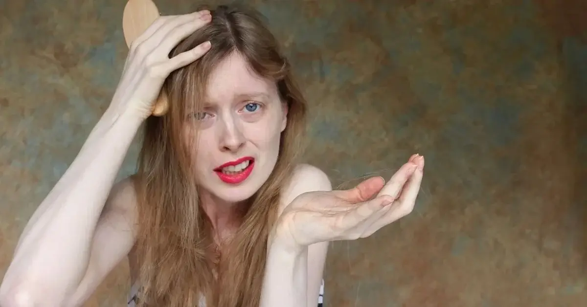 Rozczochrana kobieta trzymając w ręku szczotkę w rozpaczliwym geście szuka sposobu na wypadające włosy