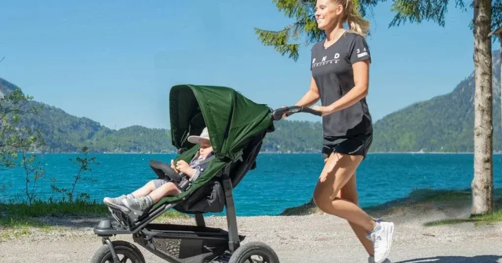 Kobieta w parku z dzieckiem w wózku sportowym uprawia jogging