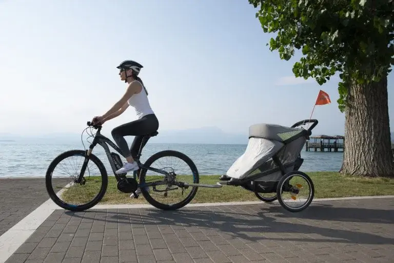 Kobieta na rowerze z przyczepką rowerową wózkiem sportowym dla dziecka
