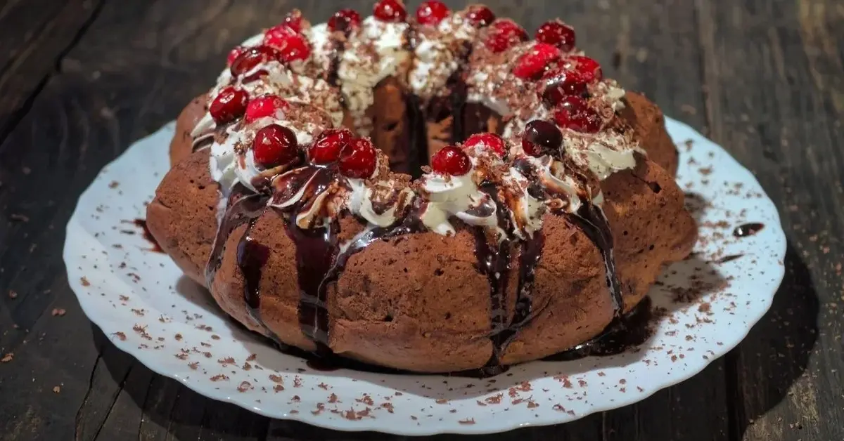 Wykwintna babka kakaowa z wiśniami, udekorowana bitą śmietaną i czekoladą