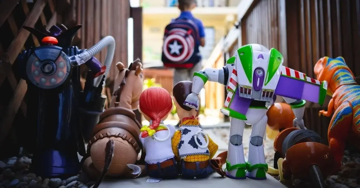 Szereg zabawek interaktywnych z fimu Toy Story ustawionych w rzędzie na chodniku spogląda za odchodzącym chłopcem